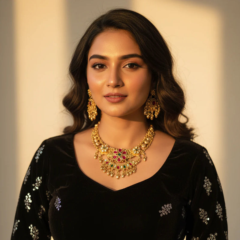 South Asian woman wearing antique gold plated temple kundan necklace set with chandbali earrings on black velvet outfit