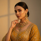 South Asian woman wearing antique gold meenakari kundan necklace set with earrings on mustard yellow lehenga