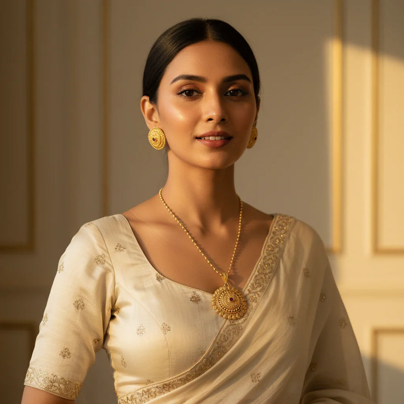 South Asian woman in cream saree wearing gold plated floral filigree medallion pendant necklace and stud earrings with ruby centre stones