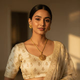 South Asian woman wearing gold plated lotus medallion pendant necklace set with stud earrings on ivory outfit
