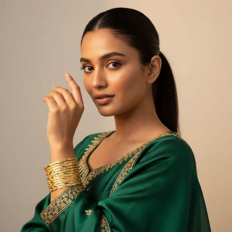 Model wearing gold plated diamond cut engraved bangles set of 8 stacked on wrist with green embroidered suit