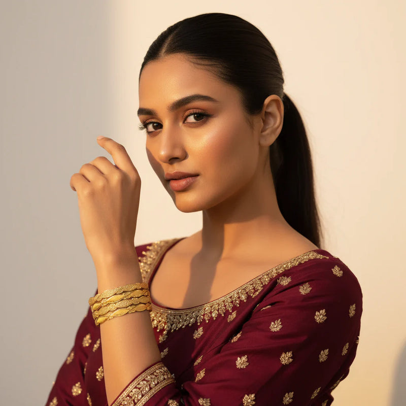 Model wearing gold plated wavy diamond cut bangles set of 4 stacked on wrist with maroon embroidered suit