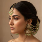 Model wearing antique gold polki bahubali jhumka earrings with mint green crystal hair chains and matching tikka wedding updo