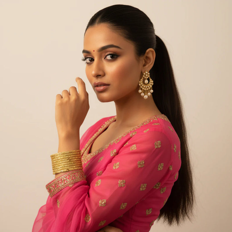 South Asian model wearing gold plated diamond cut textured bangles set of 8 stacked on wrist with hot pink embroidered outfit