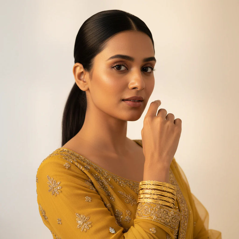 South Asian model wearing gold plated filigree medallion bangles set of 4 with mustard embroidered outfit