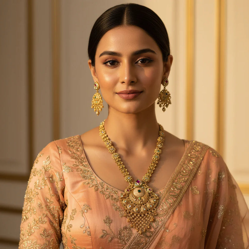 South Asian woman wearing antique gold long necklace set with ornate pendant and jhumka earrings on peach outfit