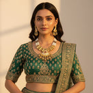 South Asian woman wearing antique gold meenakari pearl necklace set with earrings on green lehenga