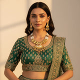 South Asian woman wearing antique gold meenakari pearl necklace set with earrings on green lehenga