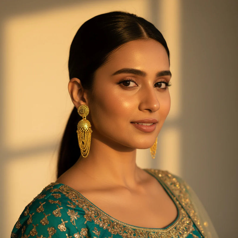 South Asian woman wearing gold plated jhumka earrings with chain tassel drops on teal lehenga