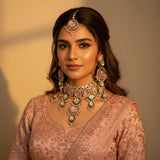 South Asian woman wearing blush pink kundan wedding choker set with earrings and tikka on pink lehenga