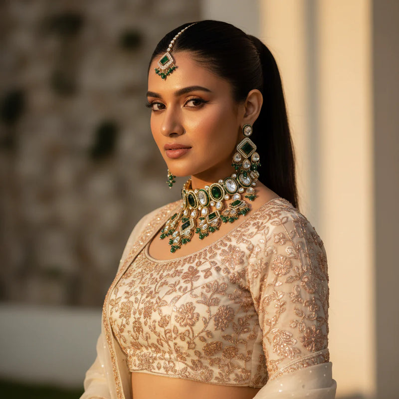 Model wearing emerald green kundan geometric choker set with earrings and tikka on ivory lehenga wedding