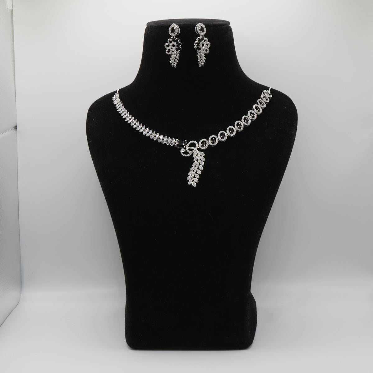 Black necklace and earrings on a black mannequin bust against a white background