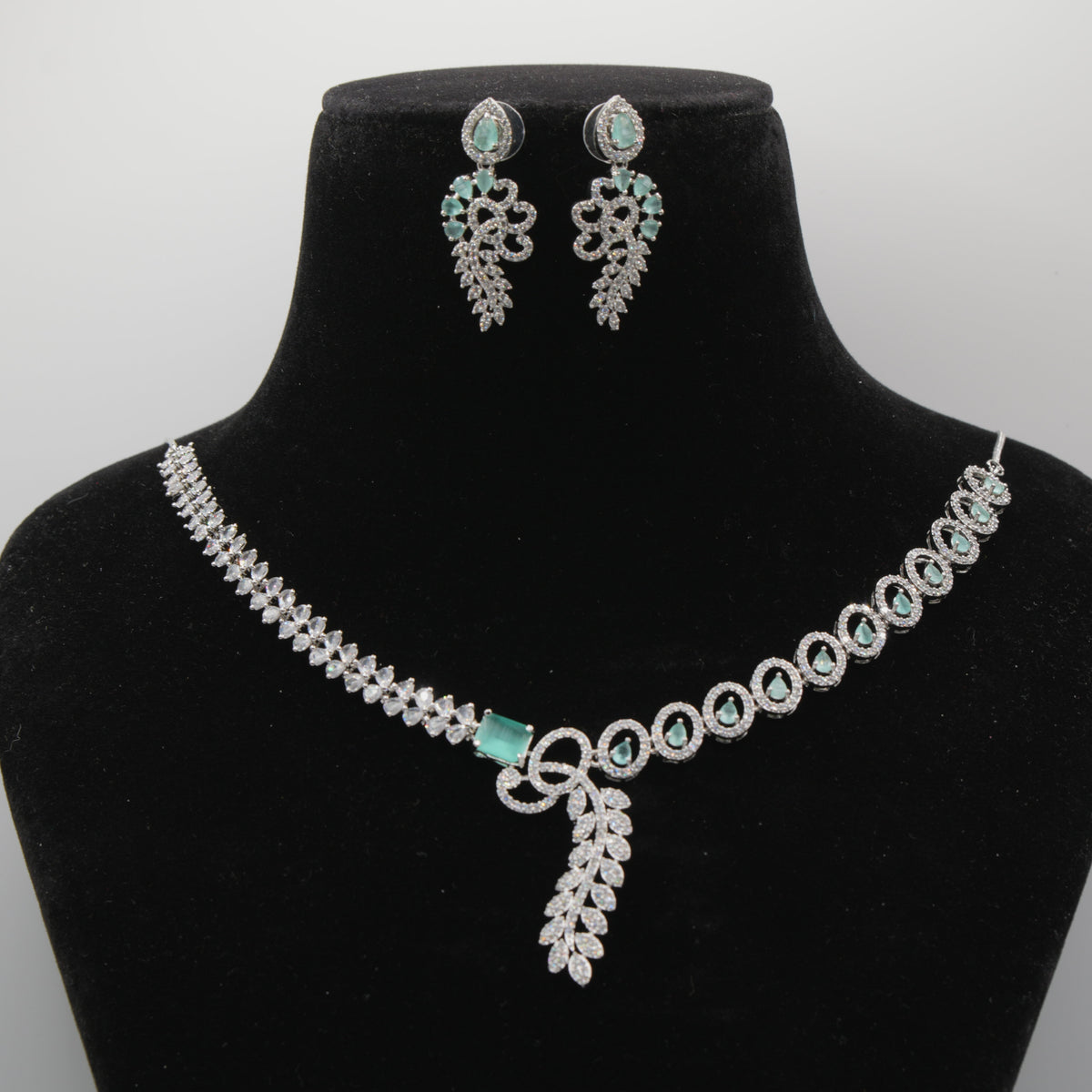 Close up of Mint diamond necklace and earrings on a black velvet bust with a gray background