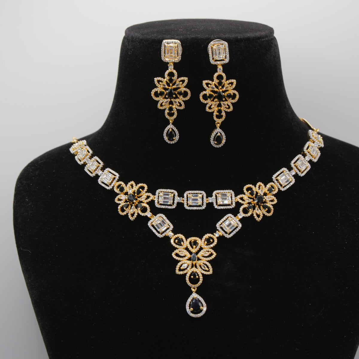 Close up of Gold and black necklace and earrings set on a black mannequin bust against a white background