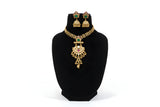 Antique gold pendant necklace set with jhumka earrings - emerald green stone variant on black display stand
