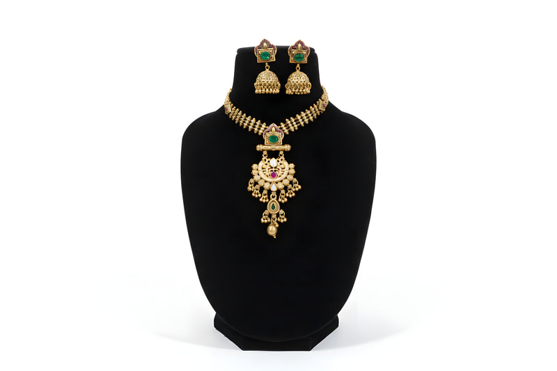 Antique gold pendant necklace set with jhumka earrings - emerald green stone variant on black display stand