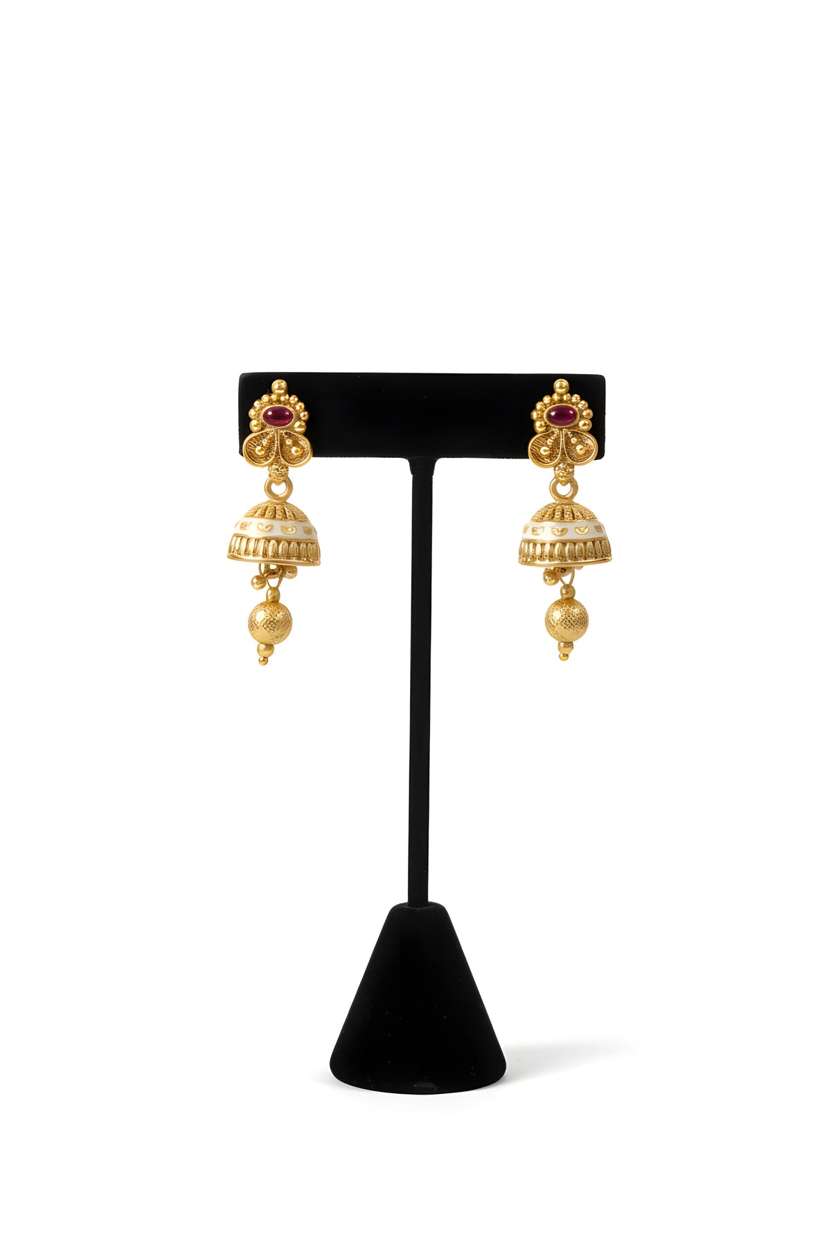 Close up of gold plated trefoil stud jhumka earrings with ruby accent white enamel dome and gold ball drop